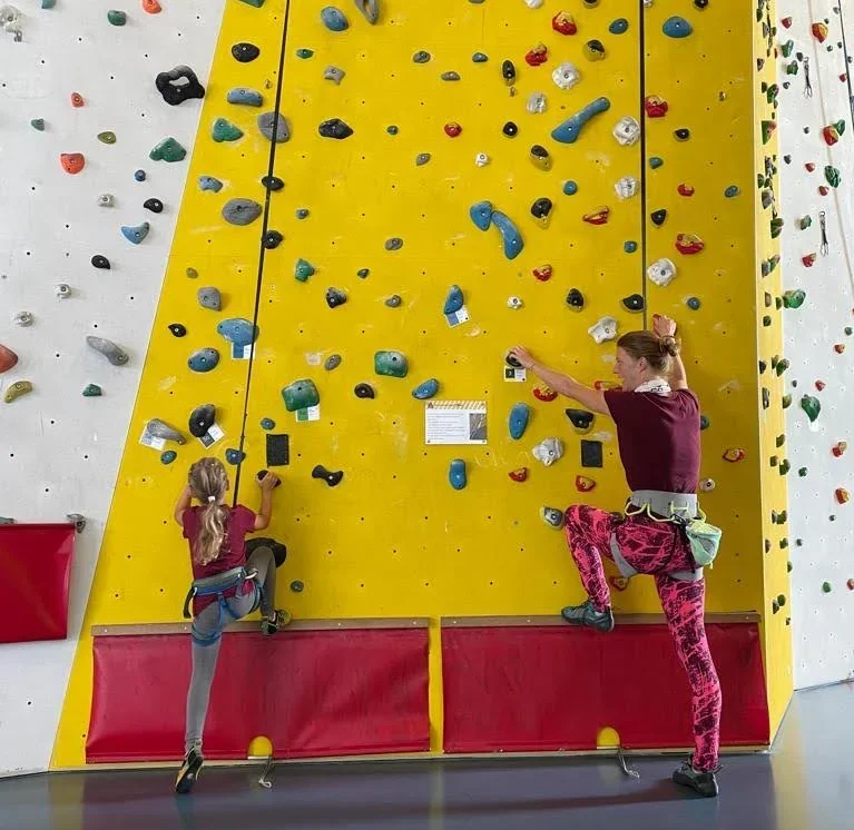 Kind und Sarah Schwegler klettern gemeinsam an gelber Kletterwand