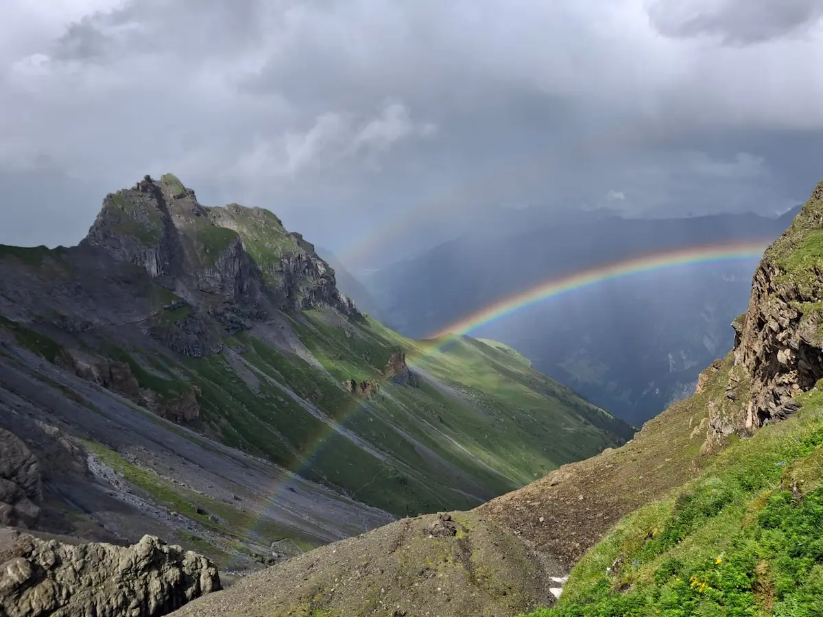 regenbogen Regenbogen über Bergtal mit grauem Himmel und grünen Berghängen